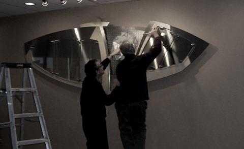 Two Men Fixing a Metallic Exhibit on the Wall