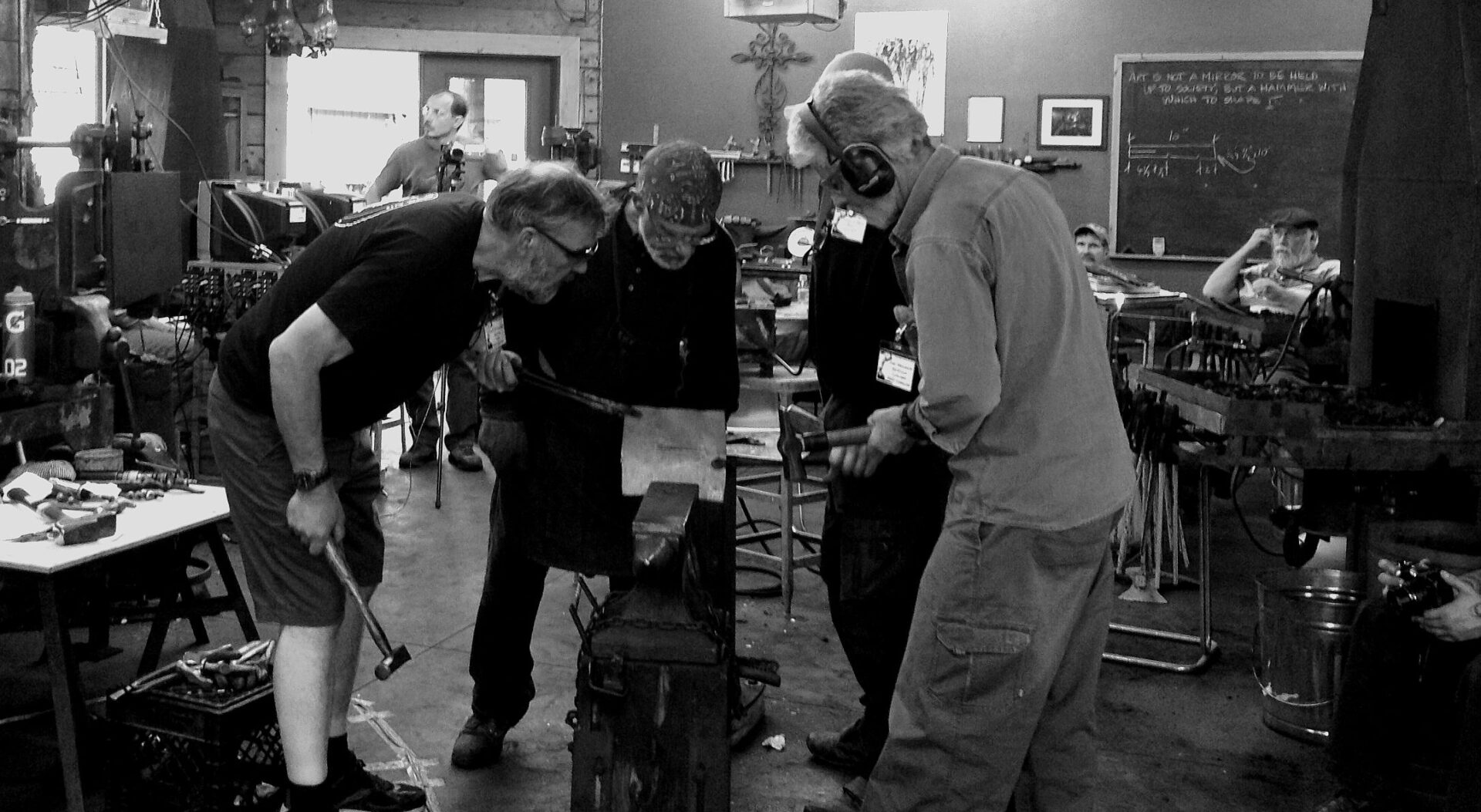 A black and white photo featuring a group of people working in a traditional blacksmith shop.