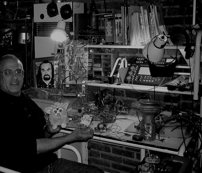 A man is sitting at a desk surrounded by various electronics during an Ira Sherman workshop.