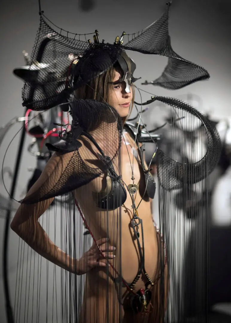 A woman in a black outfit posing in a room full of wires.
