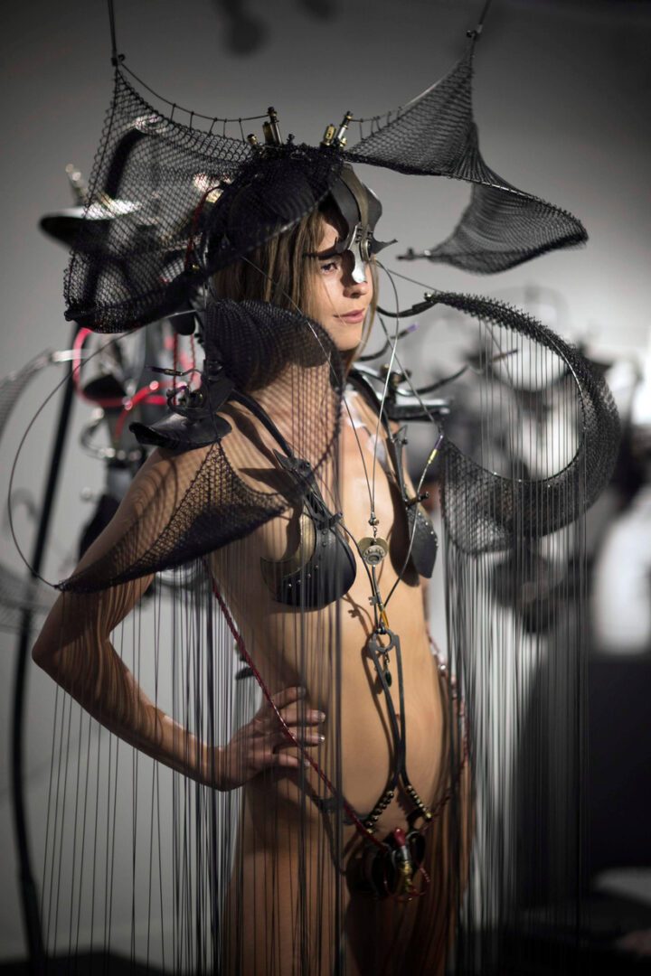 A woman in an interactive sculpture costume adorned with wires poses for a photo.