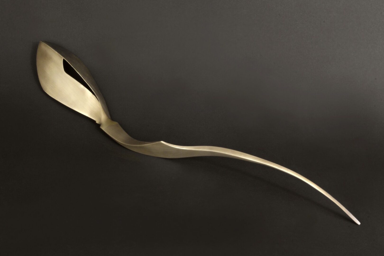 A gold swan-shaped object rests on a black surface, crafted by Ira Sherman Jewelry.