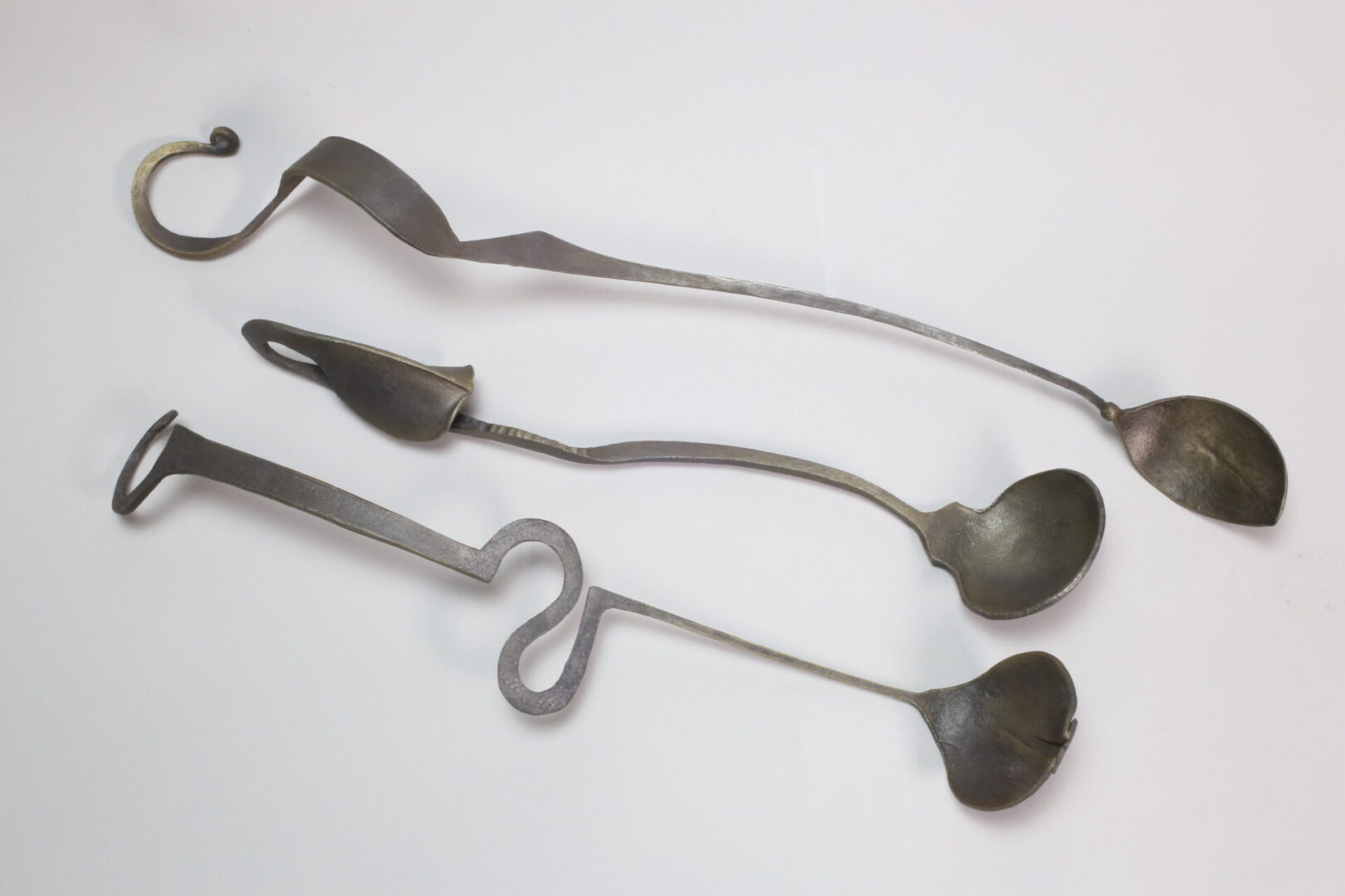 Three metal spoons on a white surface, each crafted by Ira Sherman Jewelry.